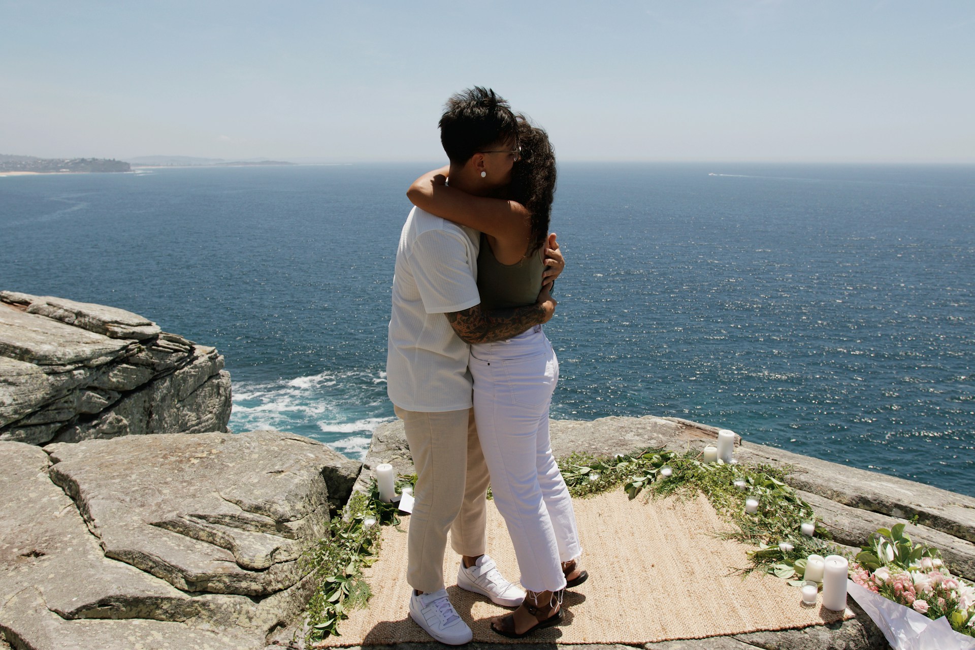 Aerial shot of a wedding ceremony set up on a scenic cliff overlooking the sparkling sea at sunset.