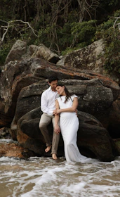 a man and a woman sitting on a rock in the water