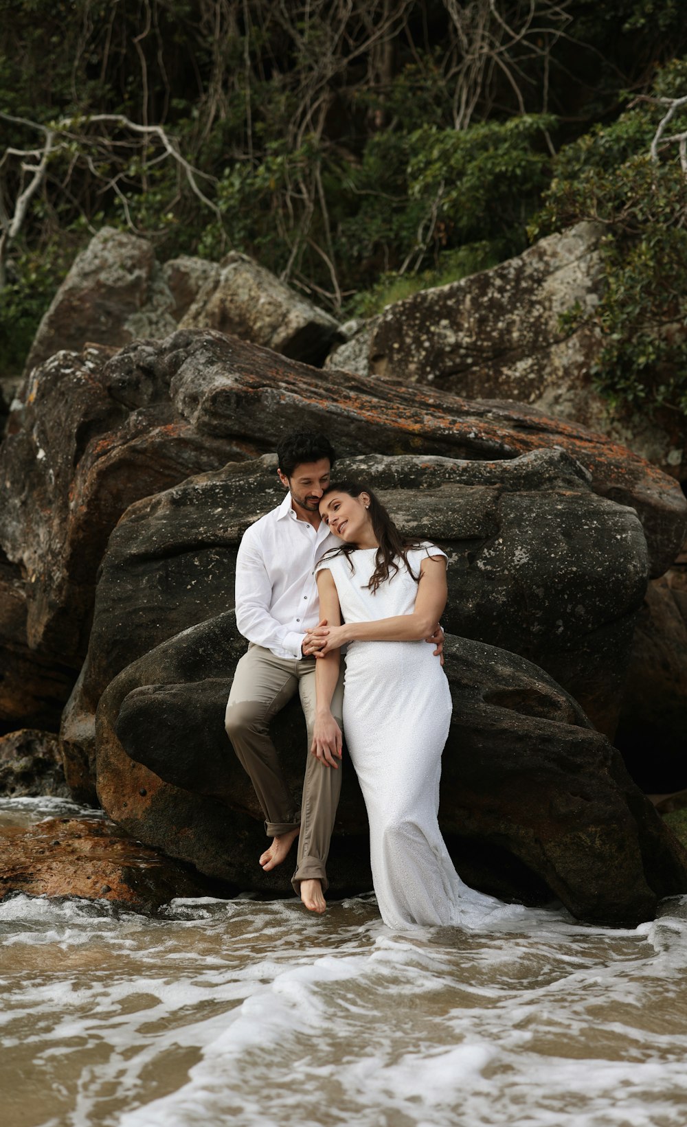 a man and a woman sitting on a rock in the water