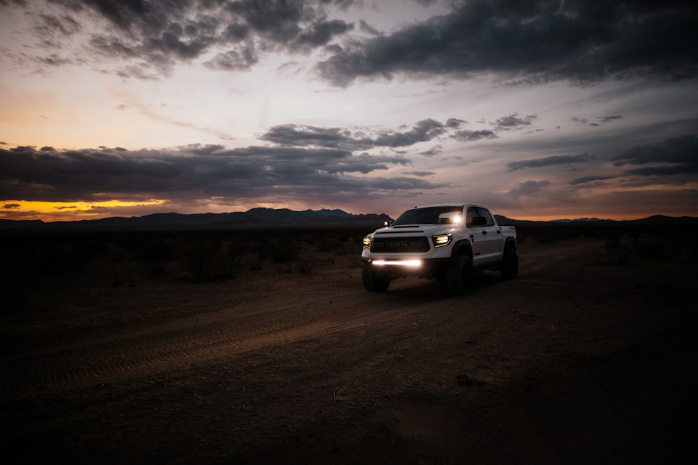 a white truck driving down a dirt road under a cloudy sky