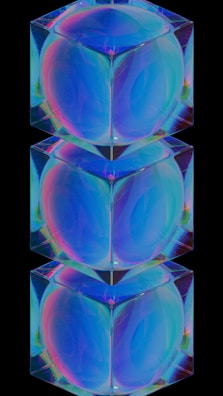 Three stacked, transparent cubes with an iridescent effect on a black background. The cubes exhibit a range of colors including blue, green, and pink, creating a holographic appearance. Each cube appears to reflect and refract light.
