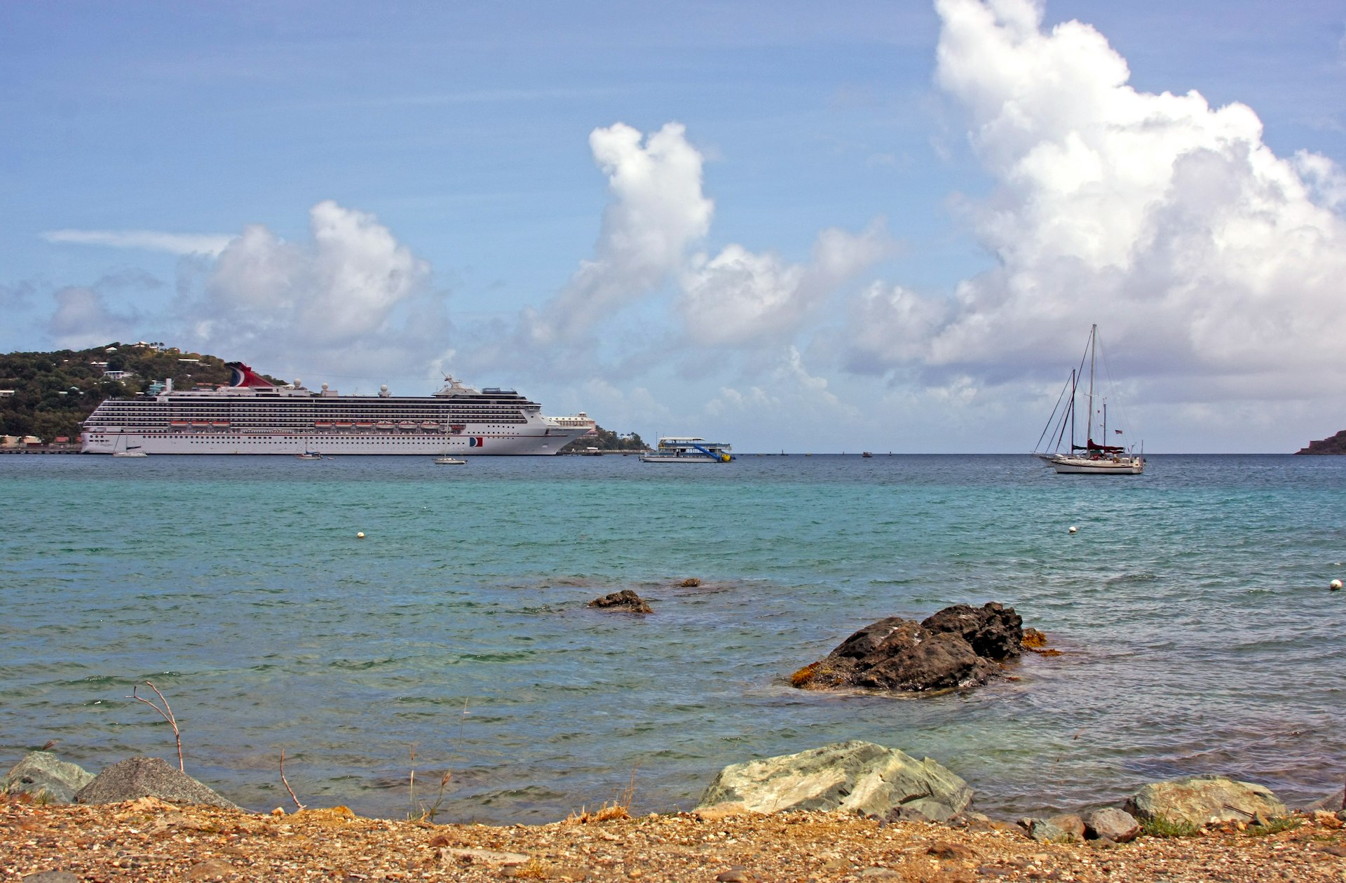 A cruise ship in the distance seen from a sunny rocky beach
