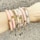 A forearm adorned with multiple beaded and metallic bracelets in various shades, including pink, white, and gold. The accessories feature different textures and designs, such as round beads and metallic elements, arranged harmoniously across the wrist.