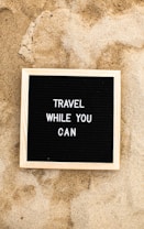 a sign that says travel while you can