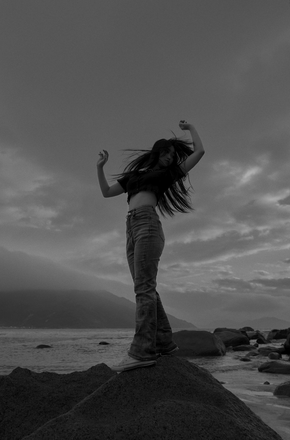 a woman standing on top of a rock near the ocean