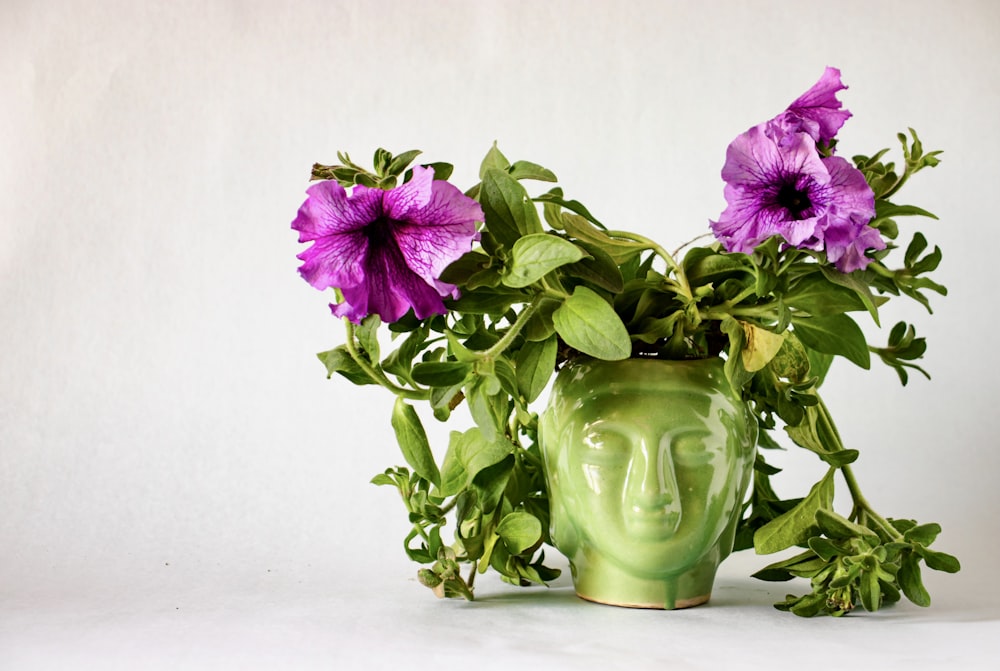 a green vase with purple flowers in it