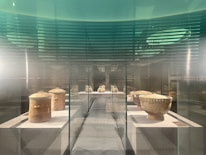 An exhibit of ancient pottery is displayed inside a transparent glass case. The pottery includes two large cylindrical jars and several round bowls, all with an aged, earthy appearance.