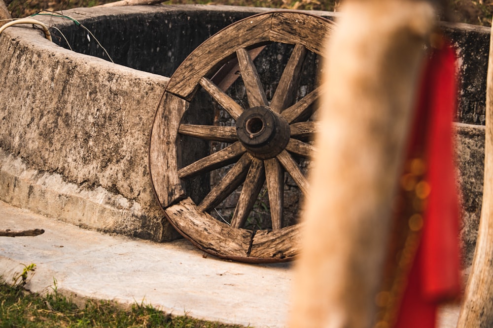 a wooden wheel sitting on top of a cement wall