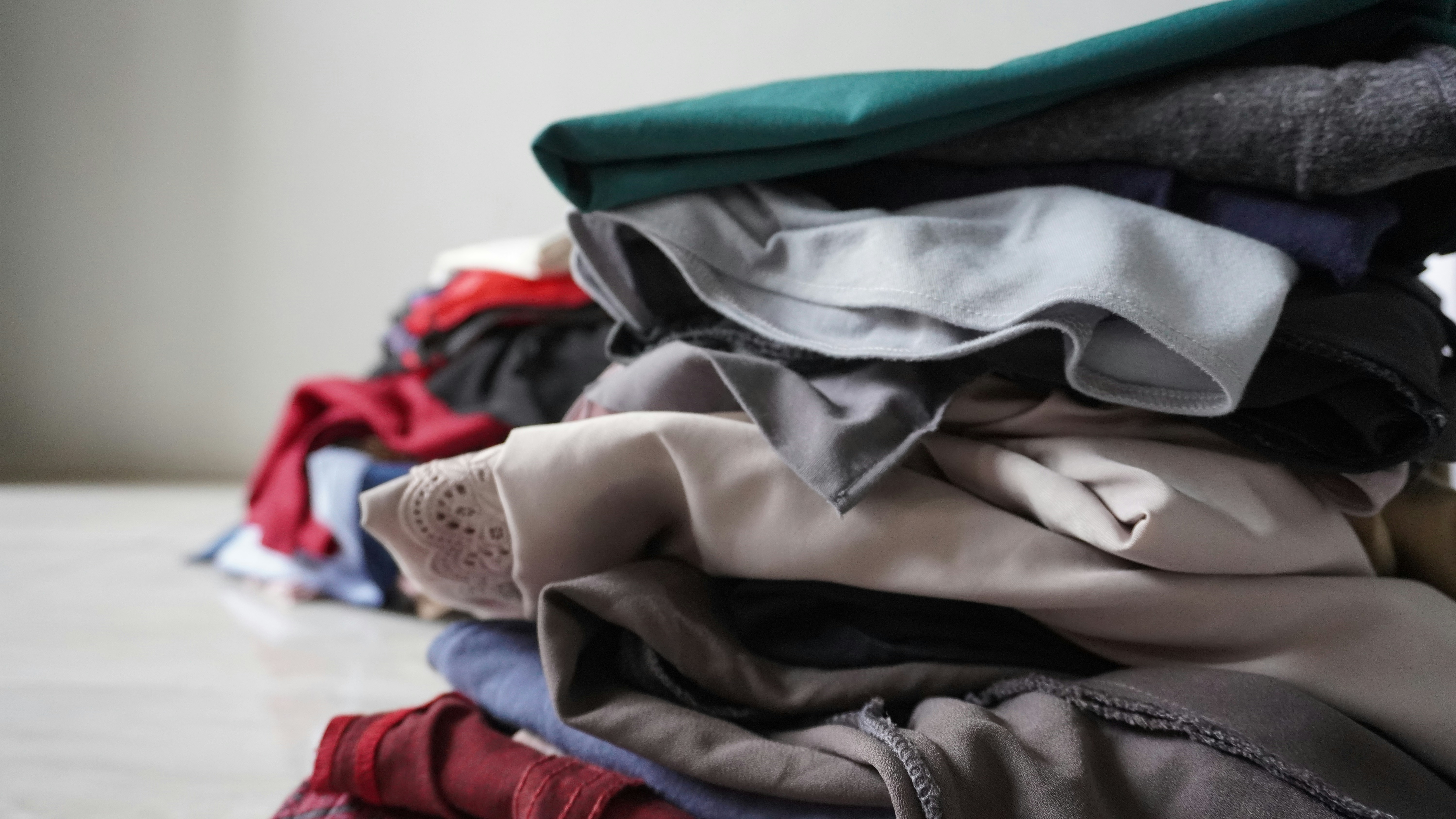 Large pile of assorted secondhand clothing in various colours — mixed garments ready for sorting, warehouse setting