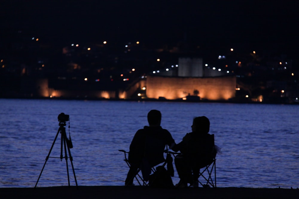 a couple of people sitting next to a body of water