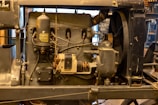 An antique engine with visible components such as gears, pipes, and a cylindrical tank. The engine has a worn, industrial appearance and is mounted on a metal frame.