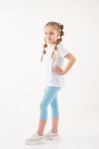 a little girl in a white shirt and blue leggings