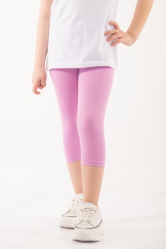 A person wearing a white top and pastel pink leggings is standing with one hand on their hip. The footwear is a pair of white sneakers with shiny details. The background is a plain, light color.