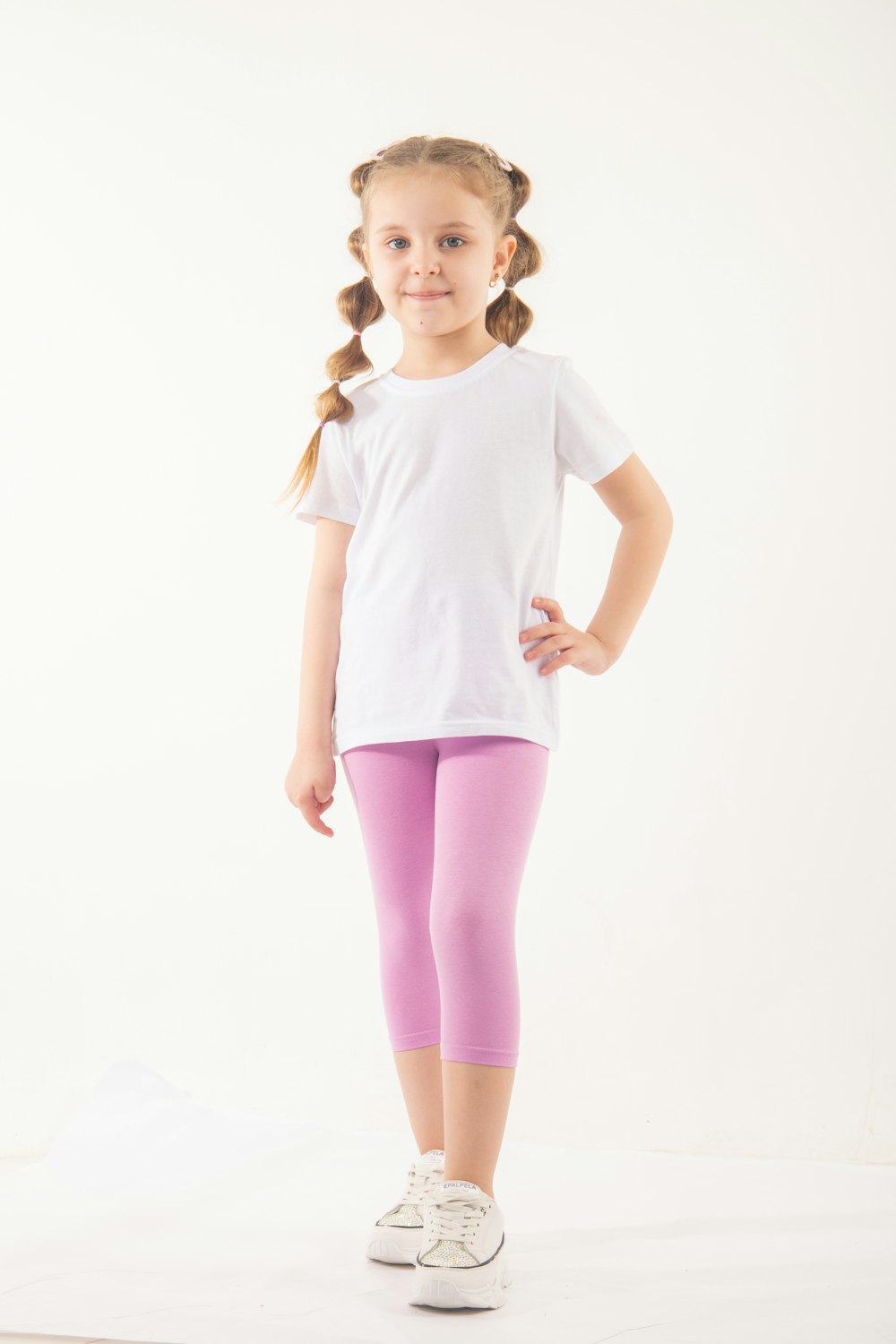 a little girl in a white t - shirt and purple leggings