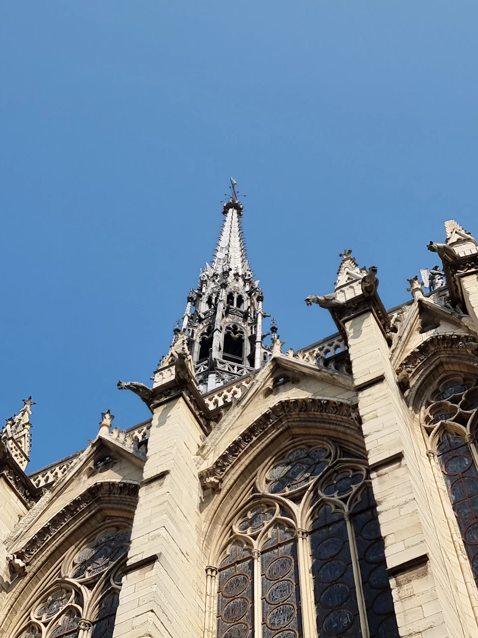 The image shows a tall, Gothic-style church with multiple spires and intricate architectural details. The church's pointed roof is adorned with numerous statues and carvings, adding to its majestic appearance. The perspective of the photo is from below, looking up at the towering structure against a clear blue sky.