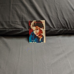 A picture of a magazine cover placed on a dark gray fabric surface. The cover features a woman with short hair, wearing a blue outfit and jewelry. The background of the cover is red.