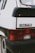 Close-up view of the rear section of a white car, focusing on the taillight and a badge labeled 'VISA 17 RD'. The car appears to have some rust and wear. The image highlights the simple and classic design elements.