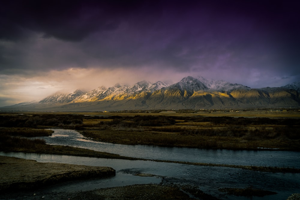 a river running through a lush green field under a cloudy sky