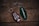 Two retro-style keychains with inscriptions are placed on a rustic wooden surface. The left keychain is maroon and reads 'CABIN IN THE WOODS 315' with a small cabin and tree illustration. The right keychain is green with the text 'ROAMNORTH' printed on it.