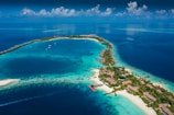 Aerial view of a tropical island surrounded by vibrant turquoise and deep blue waters. The island is dotted with lush greenery and several bungalows or villas. Boats are seen docked near the shore and small pathways connect various parts of the island. Wispy clouds are scattered across the bright blue sky.