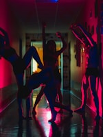 A group of people is performing dynamic dance poses in a dimly lit hallway, with silhouettes enhanced by vibrant red and blue lighting. The poses are expressive and artistic, creating a visually striking scene.