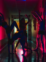 A group of people is performing dynamic dance poses in a dimly lit hallway, with silhouettes enhanced by vibrant red and blue lighting. The poses are expressive and artistic, creating a visually striking scene.