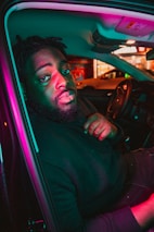 Close-up of a rider’s joyful face illuminated by neon lights inside a vehicle with music equalizer visuals in the background.