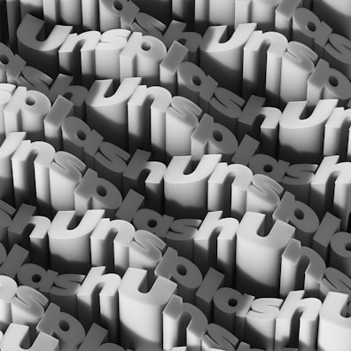 Multiple 3D text blocks repeating the word 'Unsplash' arranged in a staggered, overlapping pattern, creating a sense of depth and texture. The design features shades of gray, giving a monochromatic appearance.