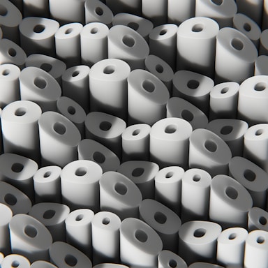 A large number of white paper rolls are tightly packed together, creating a uniform and repetitive pattern. Each roll has a circular hole in the center, and they are arranged in various orientations, contributing to the overall texture and visual interest.