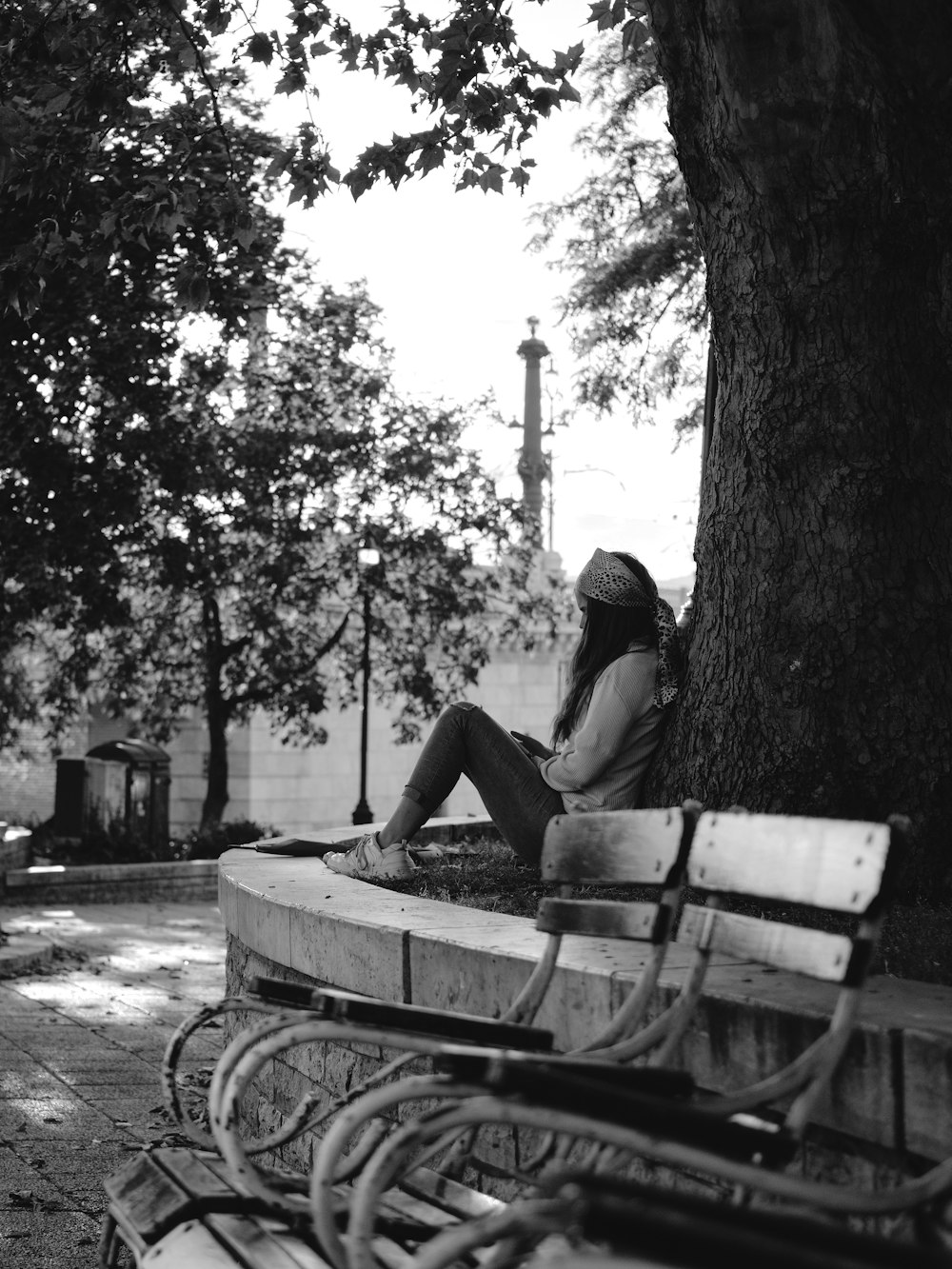 a woman sitting on a park bench next to a tree