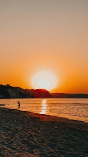 A vibrant sunset over a calm ocean horizon with a silhouette of a lone traveler standing on a cliff.
