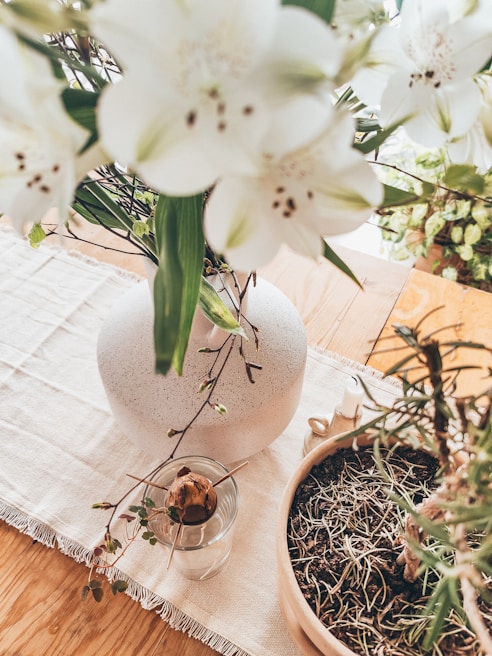 Close-up of delicate white and greenery floral arrangements on a rustic wooden table