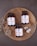 Three bottles of magnesium supplements are placed on a rustic wooden platter along with a small spoon containing white capsules. Dried flowers are arranged artfully around the bottles. The background is a textured, dark gray surface.