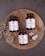 Three bottles of magnesium supplements are placed on a rustic wooden platter along with a small spoon containing white capsules. Dried flowers are arranged artfully around the bottles. The background is a textured, dark gray surface.