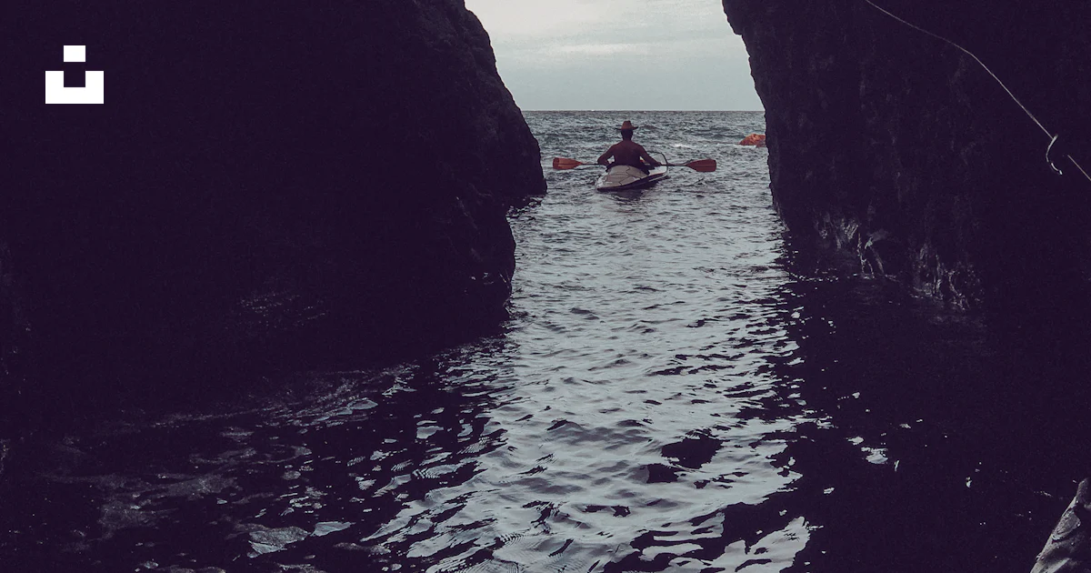 A person in a kayak in the water between two large rocks photo – Free ...