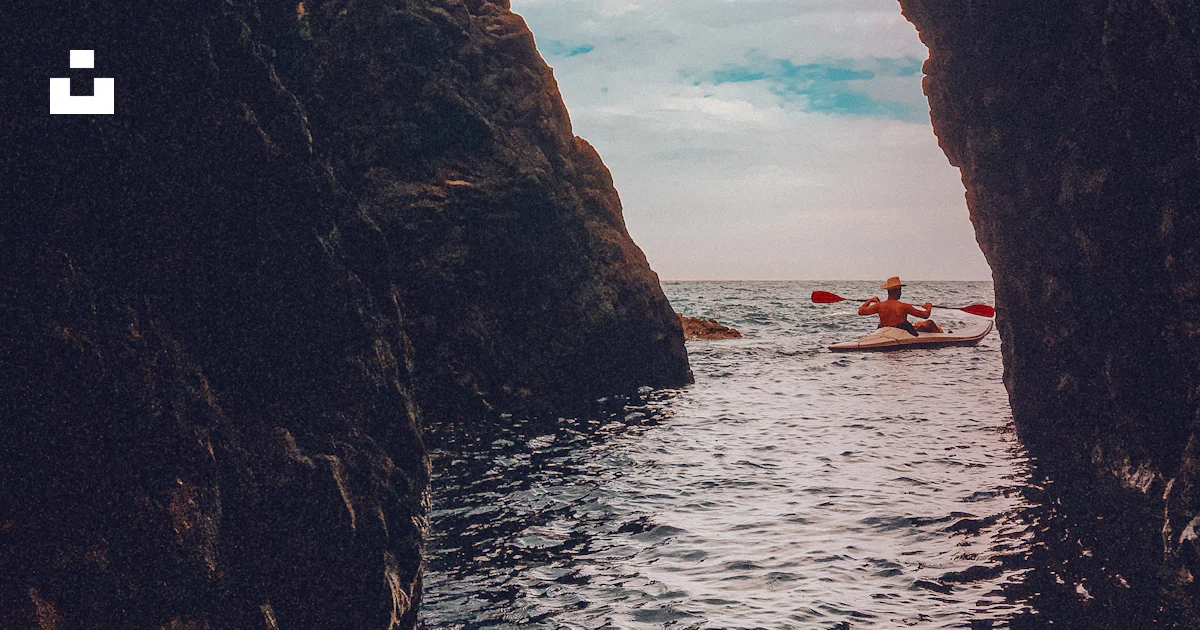 A person in a kayak in the water between two large rocks photo – Free ...