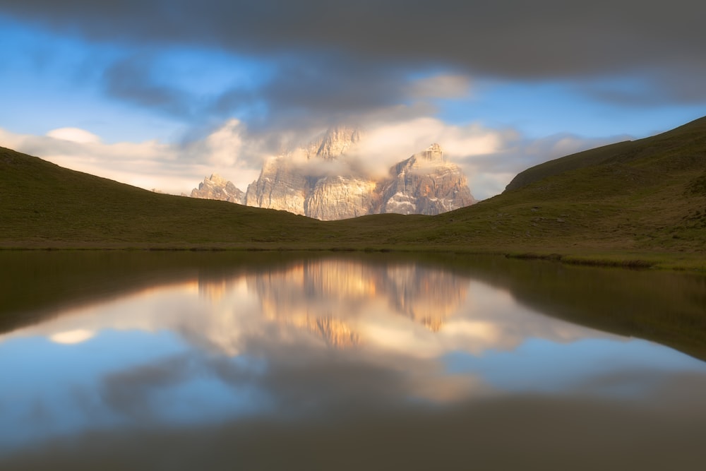 a lake surrounded by mountains under a cloudy sky