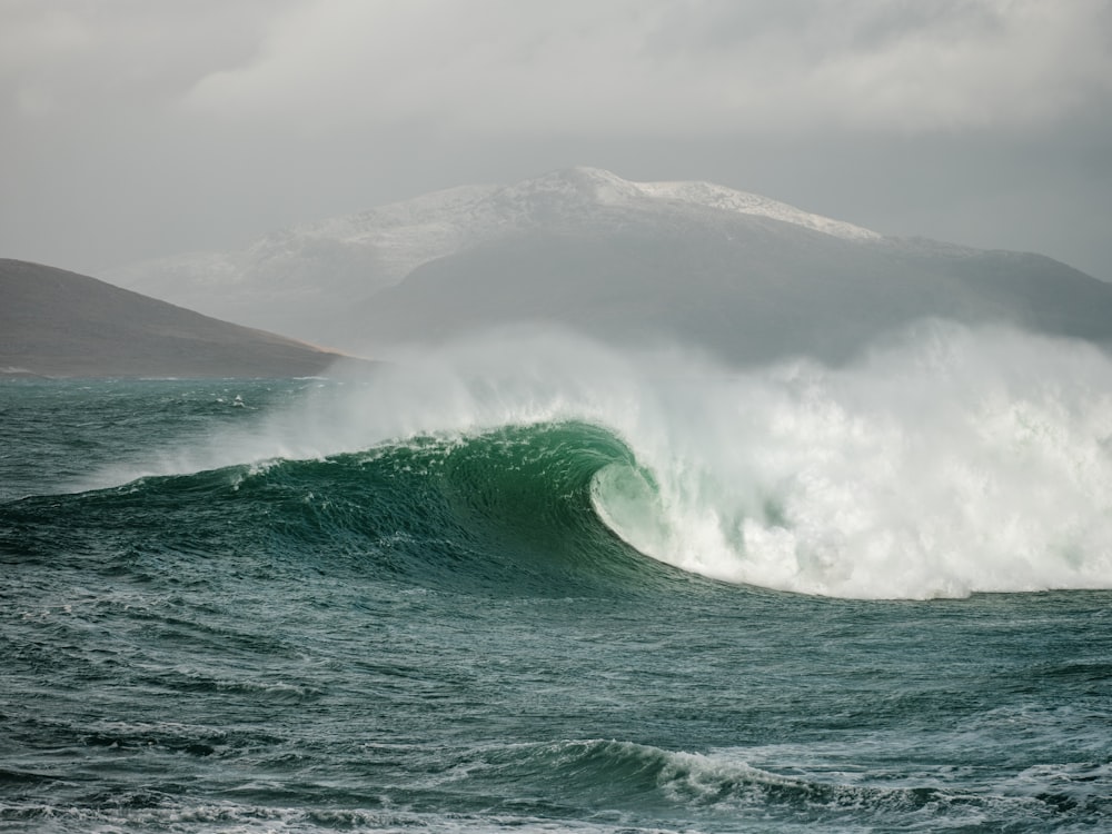a large wave in the ocean with a mountain in the background