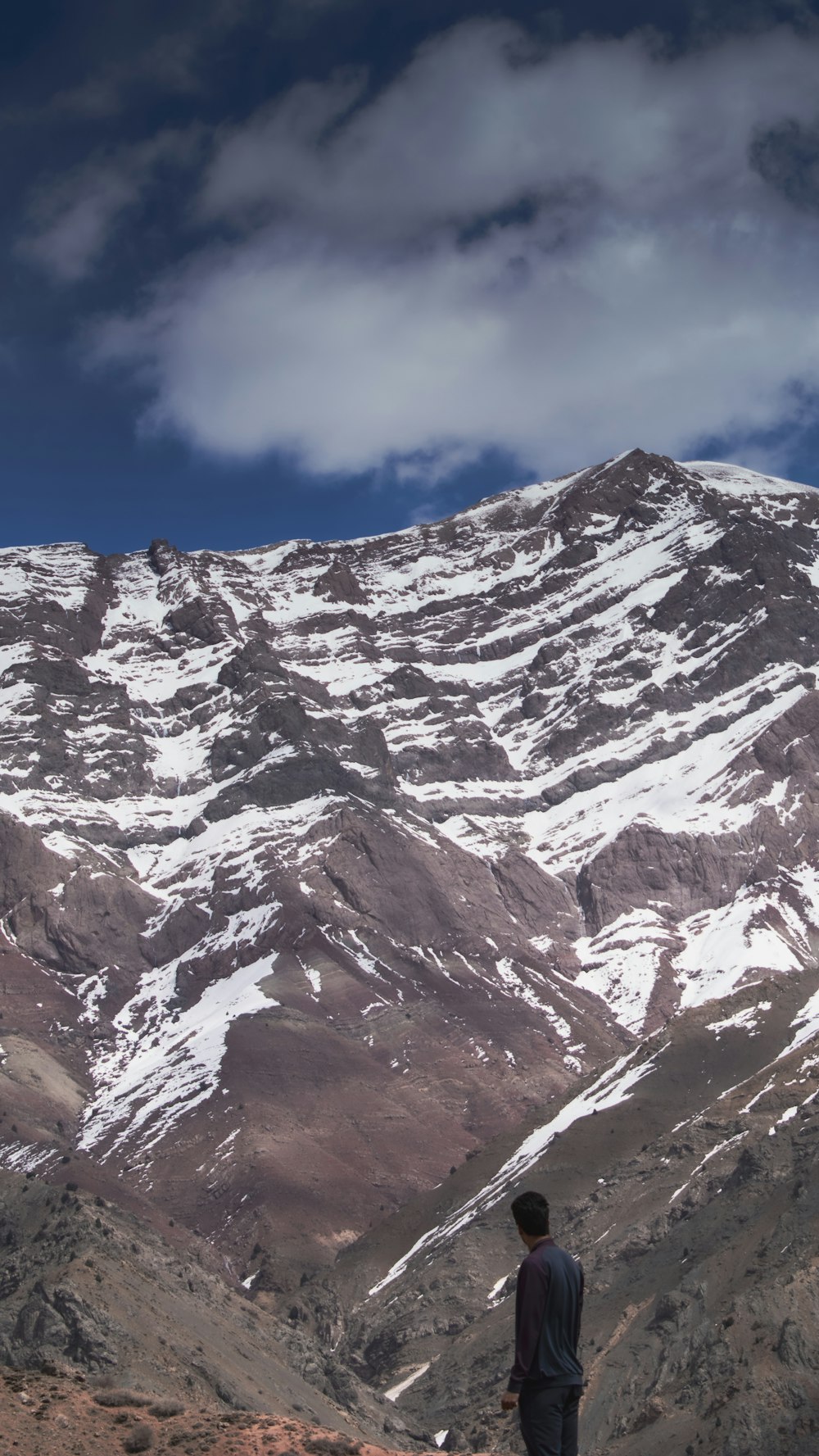 a man standing on top of a mountain next to a snow covered mountain