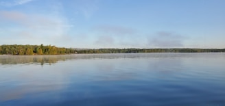 A calm lake reflecting muted blue skies, framed by gentle greenery.