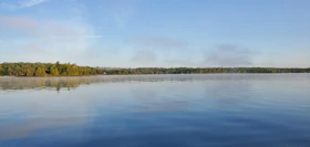 a calm lake at dawn reflecting the blue sky and surrounding lush greenery in Belarus