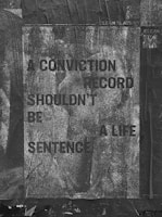 A weathered poster with text that reads 'A CONVICTION RECORD SHOULDN'T BE A LIFE SENTENCE' is displayed. The background is textured with a grayscale, worn look, and the poster appears to be pasted on a rough, dark surface. Some QR codes and text related to 'Clean Slate' are visible.
