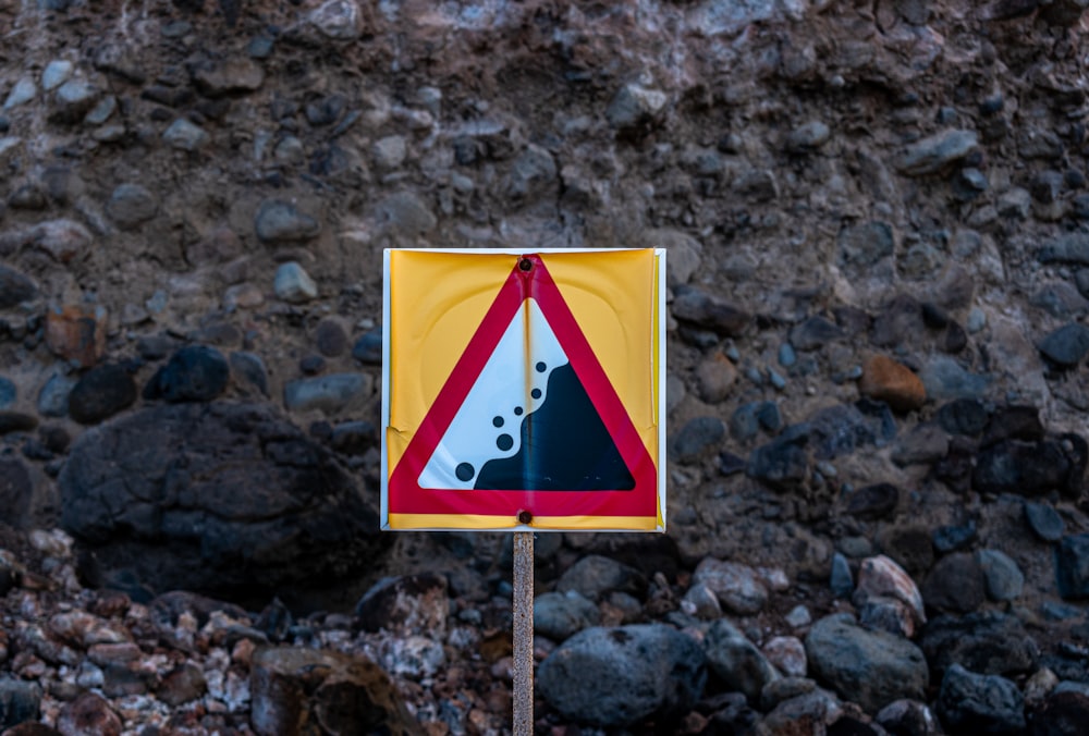 a yellow and red sign sitting on top of a rocky hillside