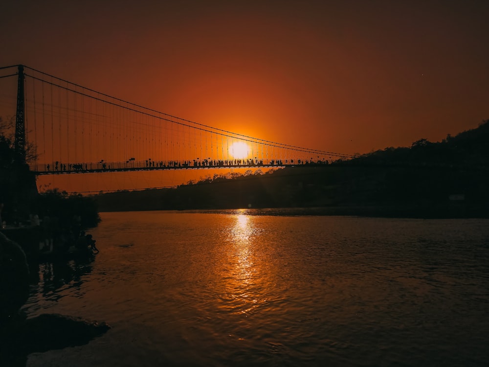 the sun is setting over a bridge over a body of water