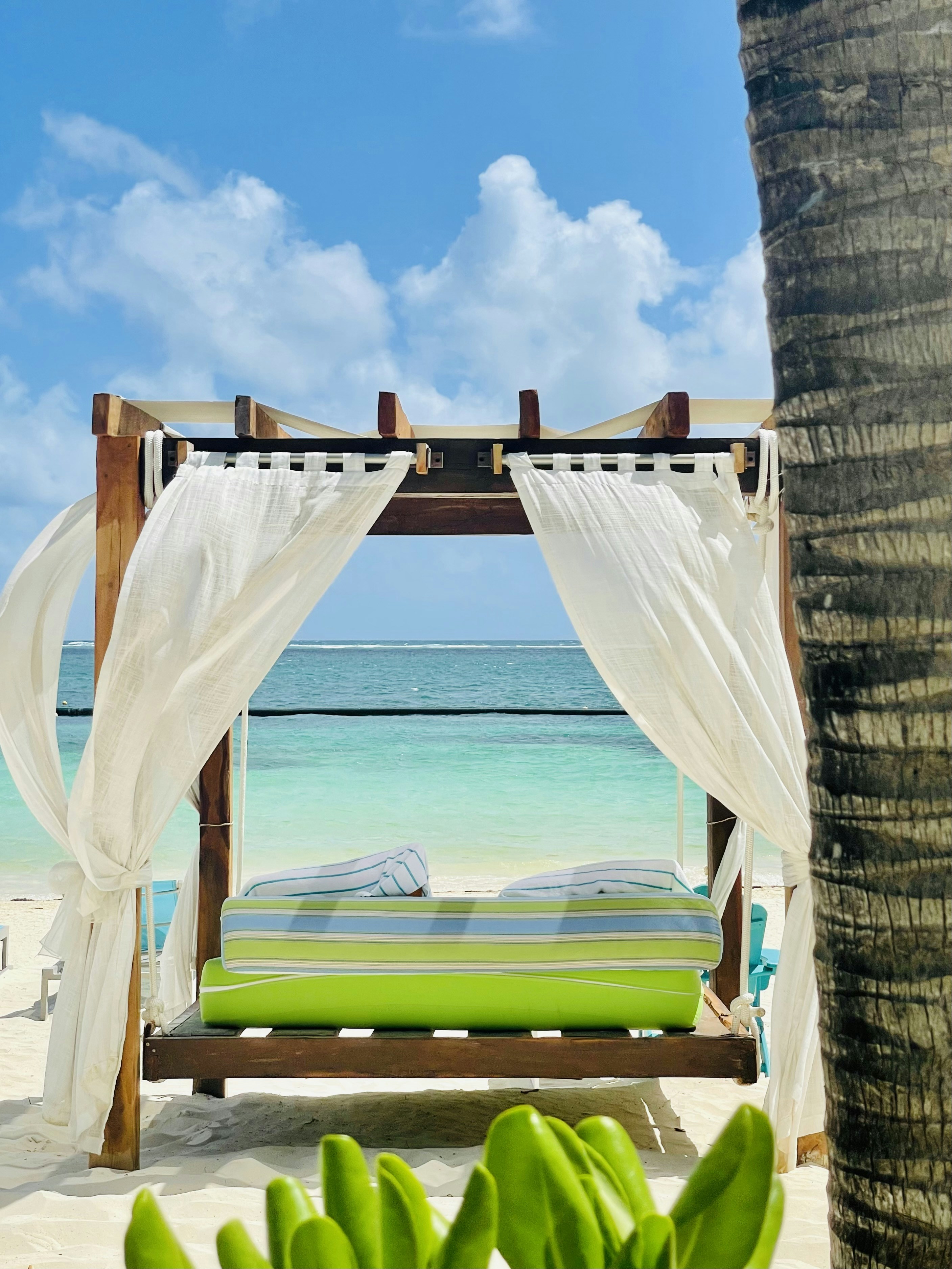 a bed sitting on top of a sandy beach under a palm tree