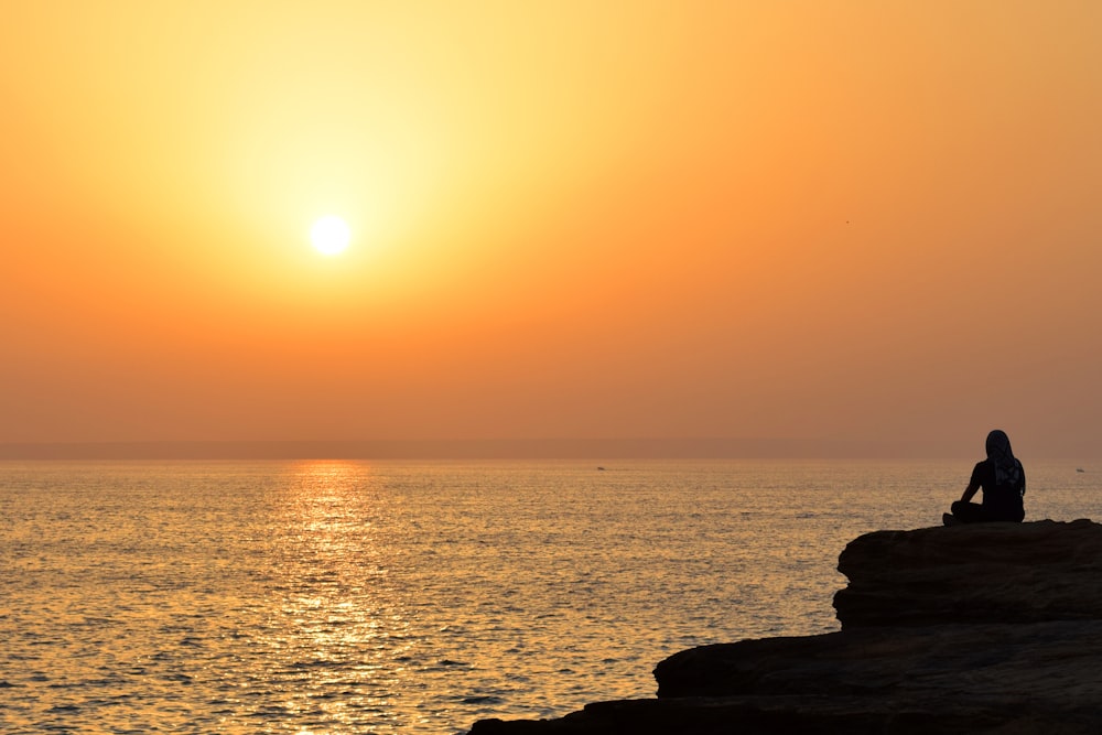 a person sitting on a rock watching the sun set