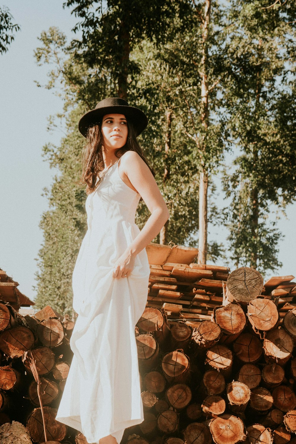 a woman in a white dress and hat standing in front of a pile of logs