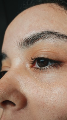 A close-up view of a person's eye and eyebrow, featuring natural skin texture, fine eyelashes, and well-defined eyebrows.