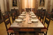 An elegant dining table with intricate hand carvings, set with fine china and golden accents in a grand dining hall.