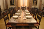 An elegant dining table with intricate hand carvings, set with fine china and golden accents in a grand dining hall.